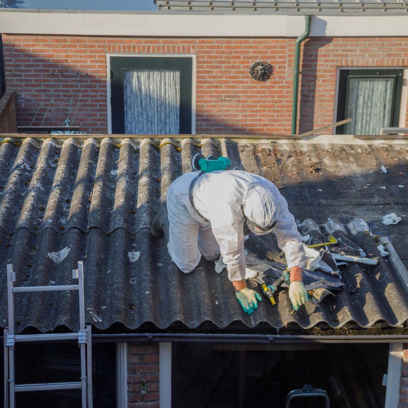 Professional asbestos removal. Men in protective suits are removing asbestos cement corrugated roofing